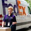 A female FedEx Express courier in uniform standing in front of FedEx van